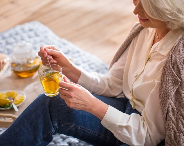 woman sitting down stirring a cup of herbal tea