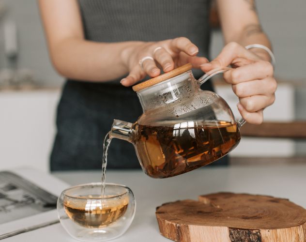 woman pouring herbal hemp tea from a brewed glass pot into a glass mug
