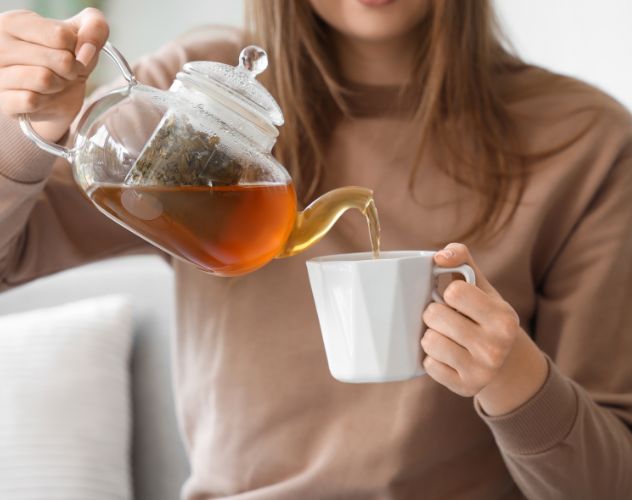 woman pouring herbal tea from teapot into mug